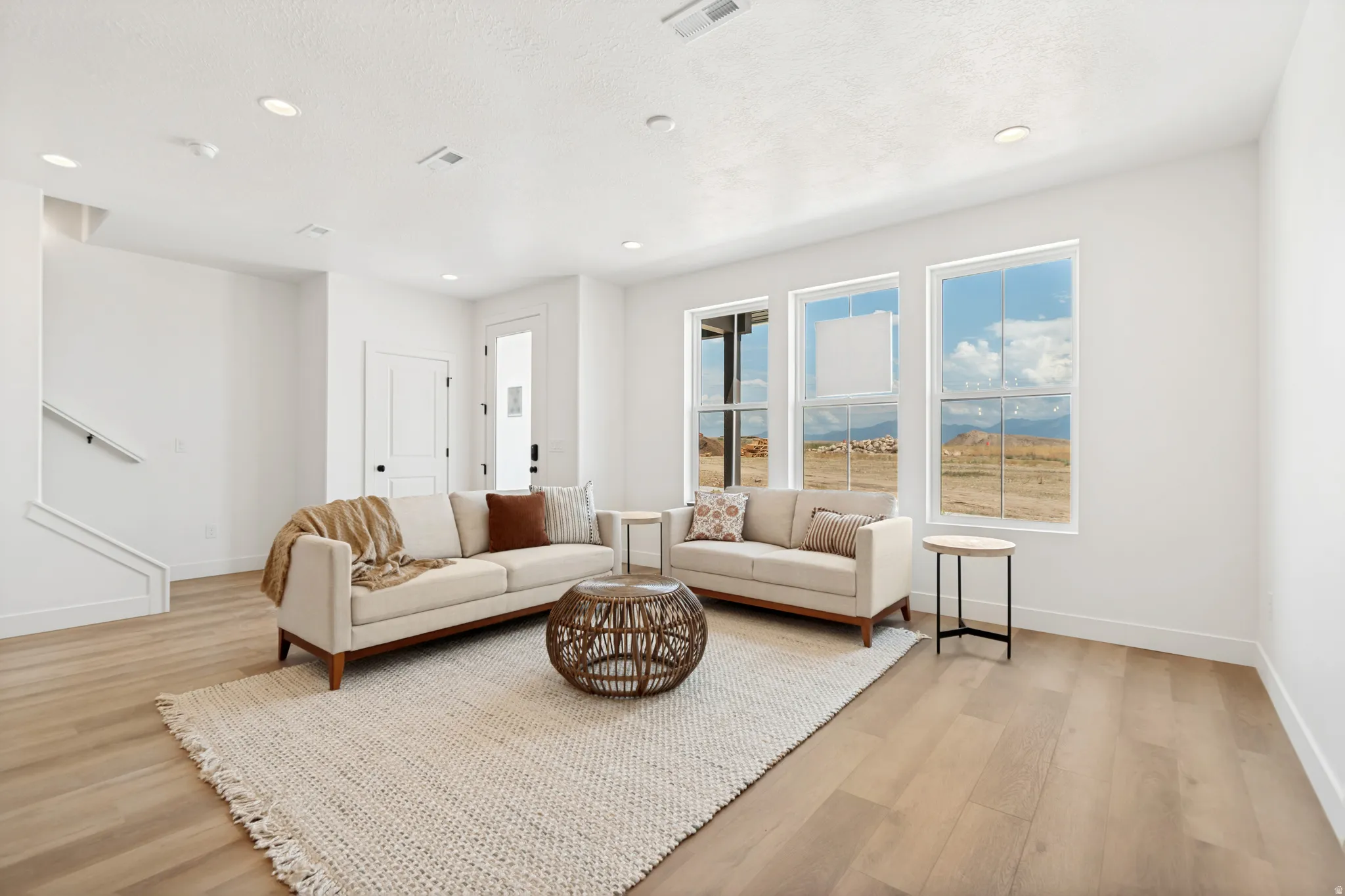 Recessed ceiling lighting, multiple large windows, wood-finish flooring, a white interior door with dark hardware, and a white staircase with a handrail