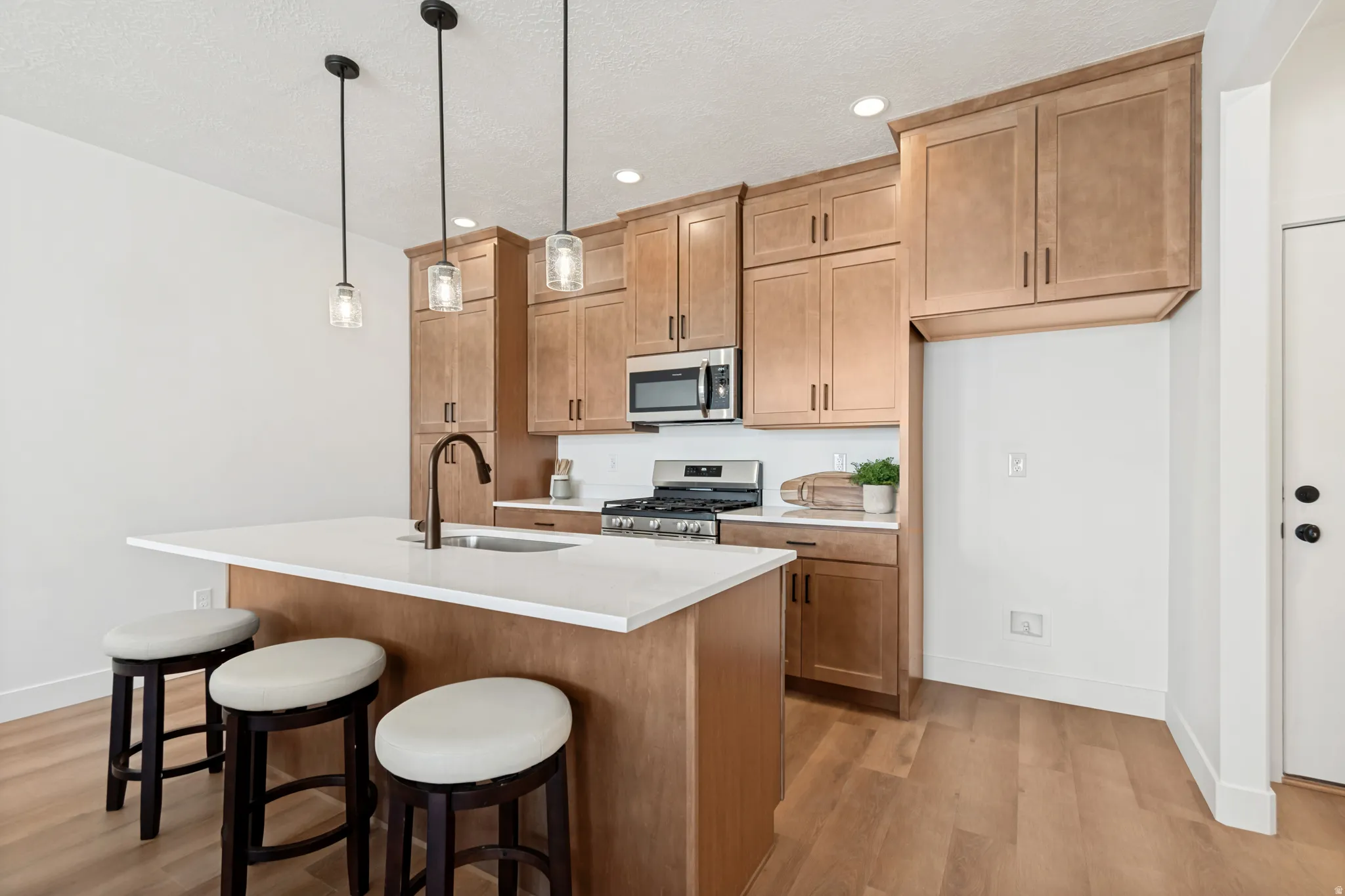 Open-concept kitchen featuring wood-finish flooring, light-toned cabinetry, stainless steel appliances, white subway tile backsplash, and a central island with a sink and pendant lighting