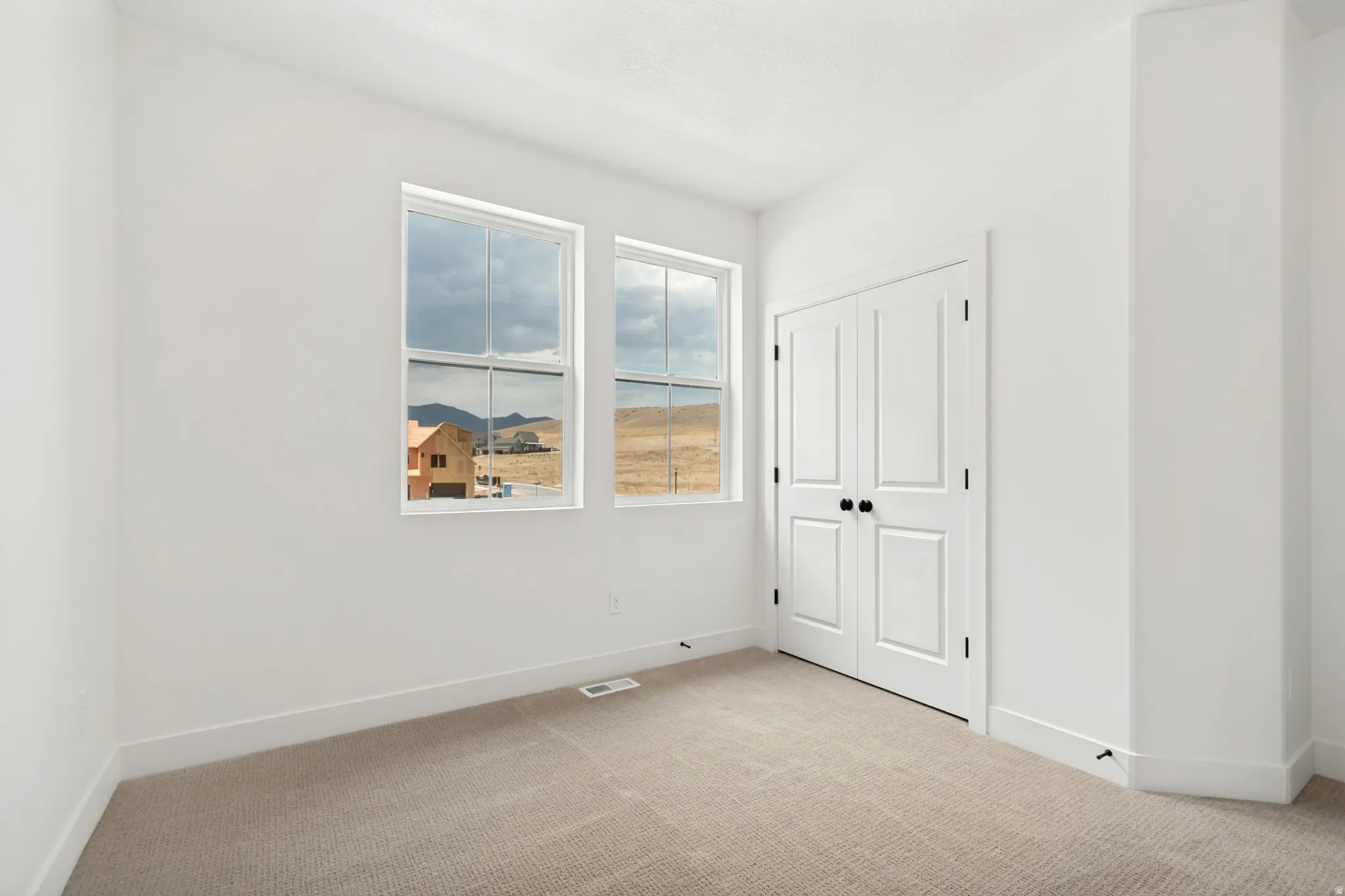 Two double-hung windows, neutral-toned carpeting, white walls, and a bi-fold closet door with black hardware