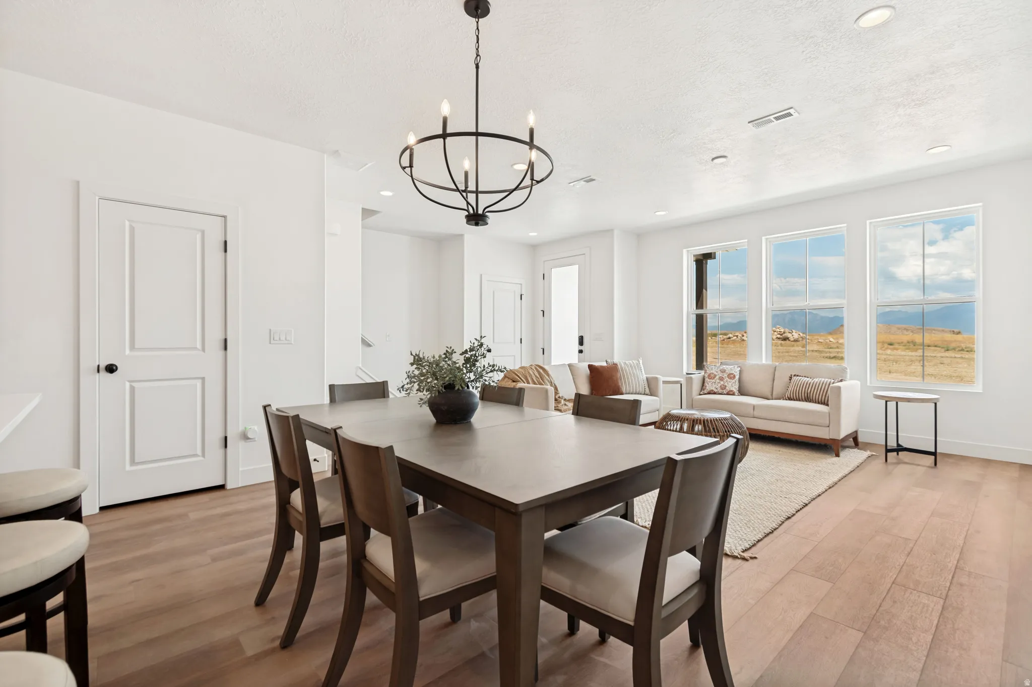 Open-concept living area featuring light wood-finish flooring, recessed lighting, and a contemporary black chandelier