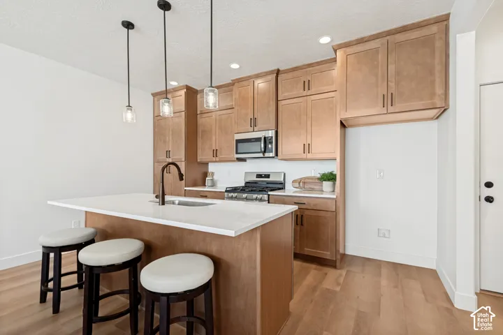 Open-concept kitchen featuring wood-finish flooring, light-toned cabinetry, stainless steel appliances, white subway tile backsplash, and a central island with a sink and pendant lighting