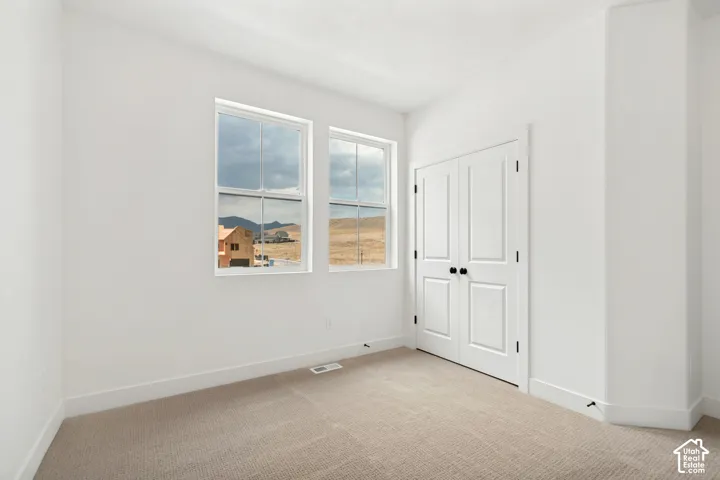 Two double-hung windows, neutral-toned carpeting, white walls, and a bi-fold closet door with black hardware