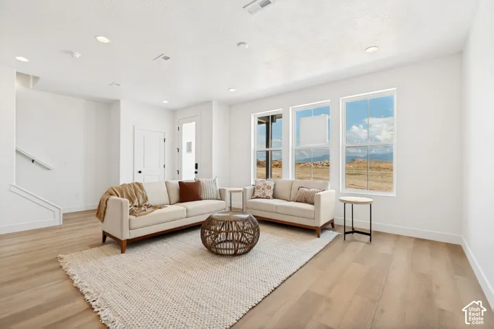 Recessed ceiling lighting, multiple large windows, wood-finish flooring, a white interior door with dark hardware, and a white staircase with a handrail