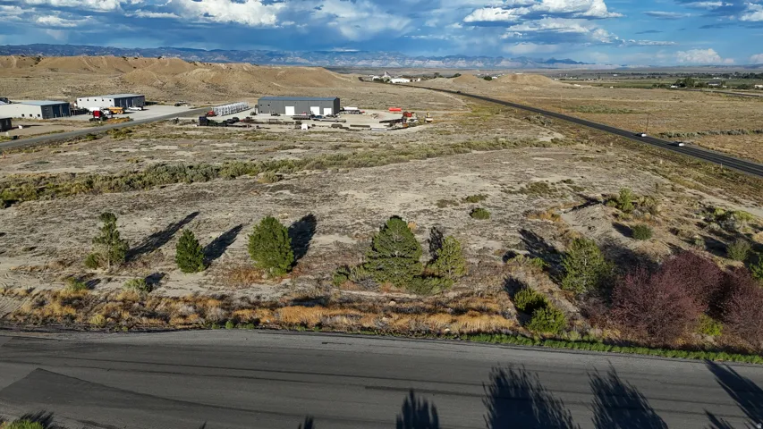 Expansive undeveloped land featuring natural desert vegetation, a paved road frontage, and distant commercial structures
