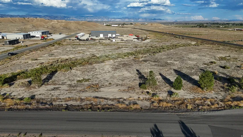 Expansive undeveloped land featuring a paved road frontage, established vegetation, and distant mountain backdrops