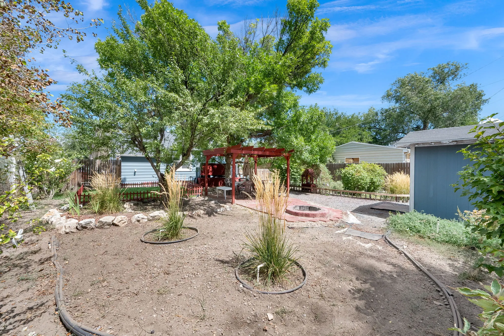 Expansive backyard featuring a red wood pergola, brick fire pit, and mature trees