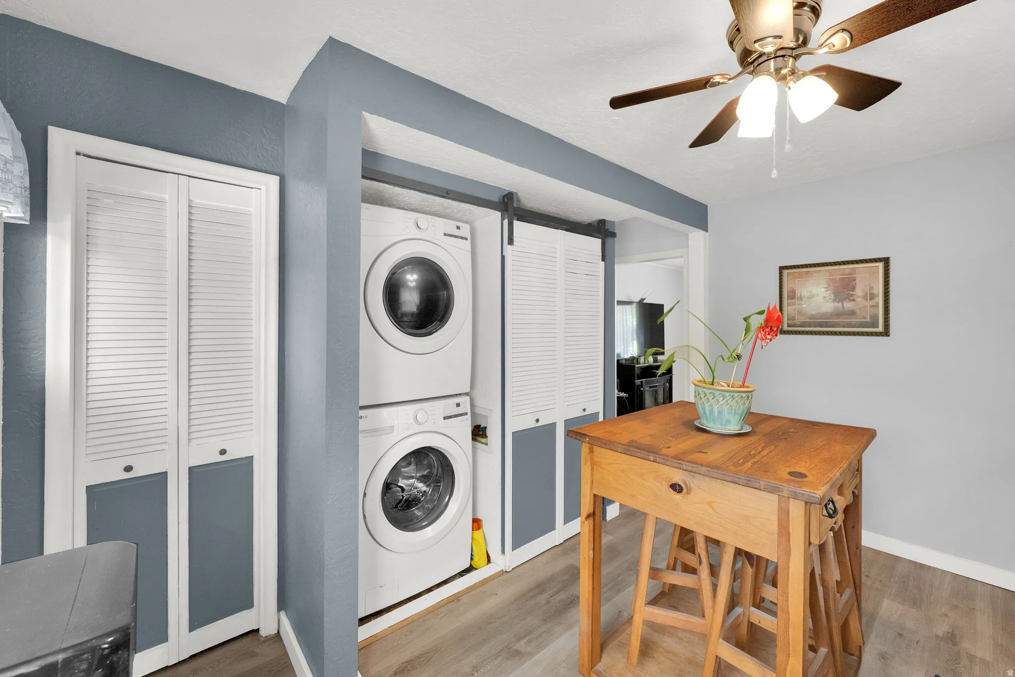 Stackable washer and dryer, wood-finish flooring, ceiling fan with integrated lighting, louvered bi-fold closet doors, and barn door style louvered doors