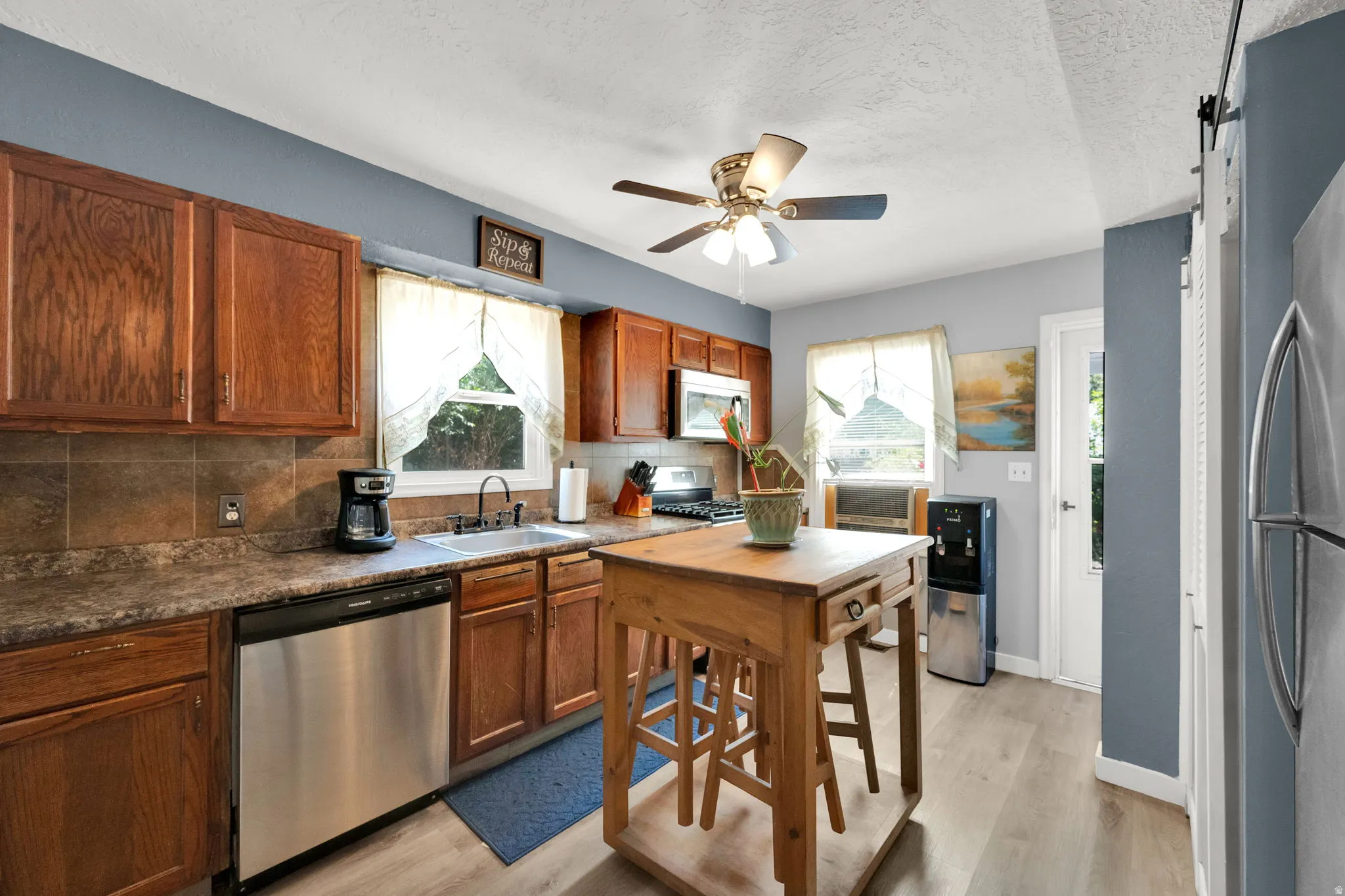 Kitchen featuring wood-finish cabinetry, stainless steel appliances, a ceiling fan, and wood-finish flooring