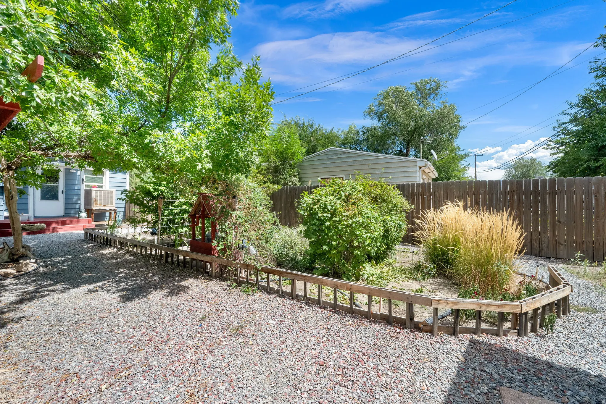 Gravel hardscaping, privacy fencing, established trees, and varied shrubbery create an inviting outdoor space