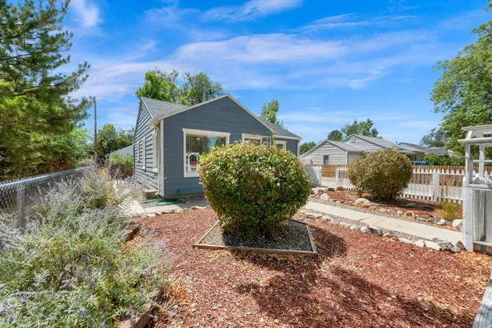 Charming residence with a dark exterior and gabled roofline, set on a landscaped lot featuring mature shrubs, decorative bark mulch, and established trees