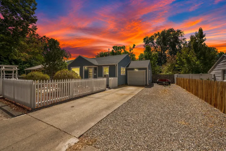 Single-story residence with a front picket fence, attached garage, gravel driveway, and wood-slat fencing