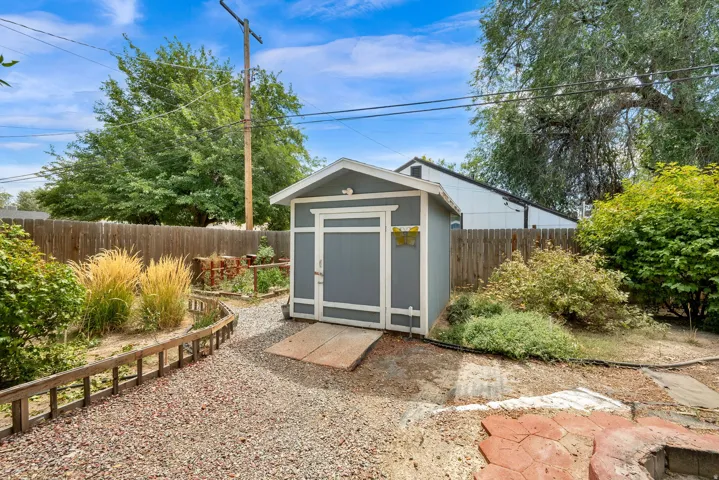 Detached storage shed with a ramp, gravel pathway, wood fencing, and established greenery
