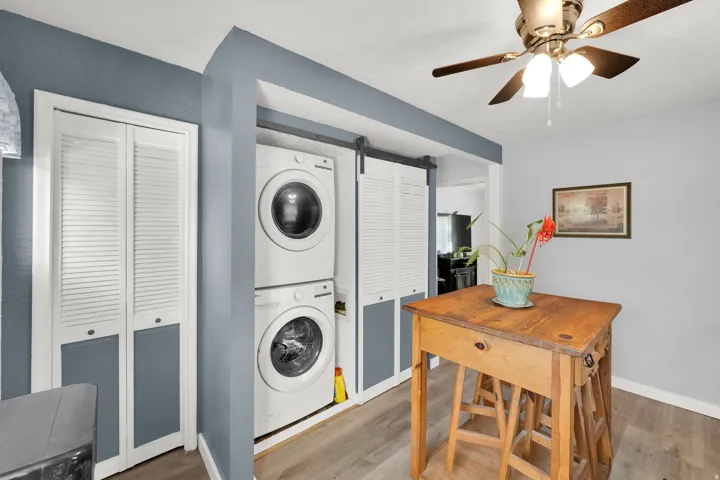 Stackable washer and dryer, wood-finish flooring, ceiling fan with integrated lighting, louvered bi-fold closet doors, and barn door style louvered doors