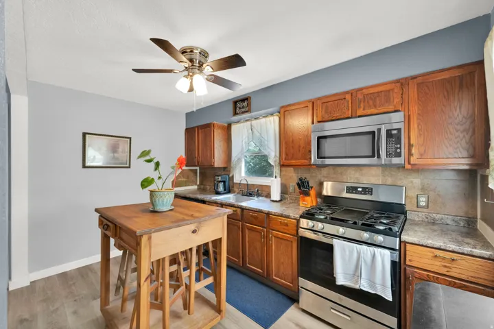 Stainless steel gas range with coordinating microwave, wood-finish cabinetry, and stone-look countertops