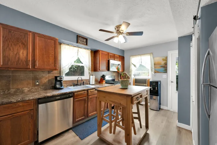 Kitchen featuring wood-finish cabinetry, stainless steel appliances, a ceiling fan, and wood-finish flooring