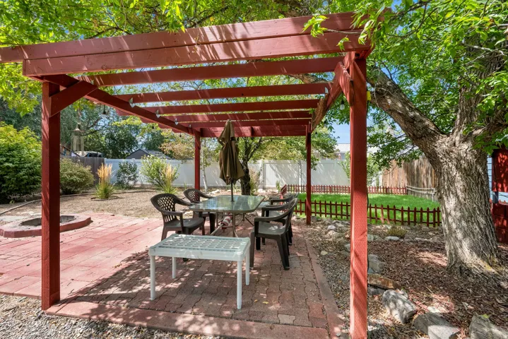 Red-stained wood pergola over a brick paver patio, featuring an integrated stone fire pit and a surrounding gravel border