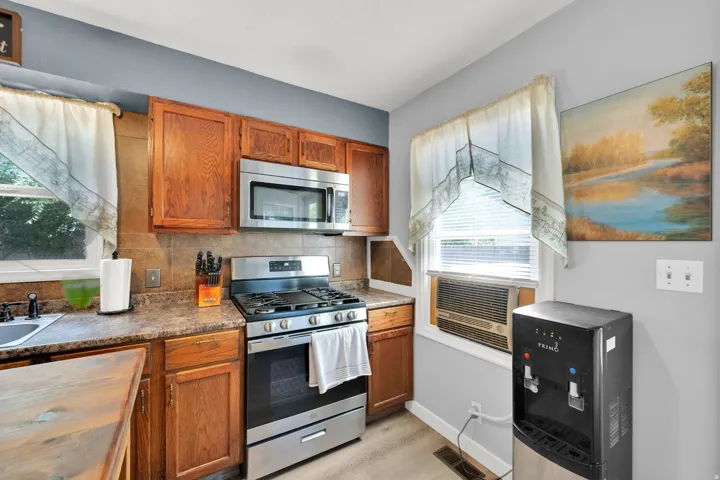 Stainless steel oven with gas range and microwave, wood cabinetry, and a tile backsplash