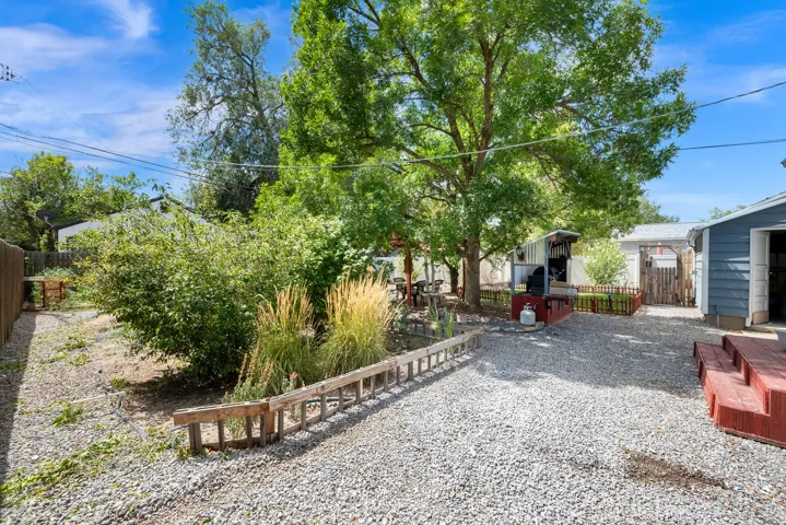 Gravel backyard featuring mature trees, established shrubs, and a distinct red-painted wooden deck