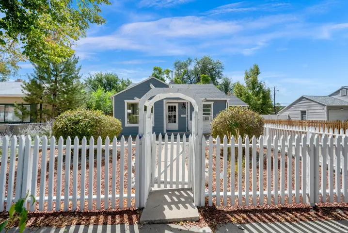 White picket fence with arched entryway, gravel landscaping, exterior painted siding, and mature plantings