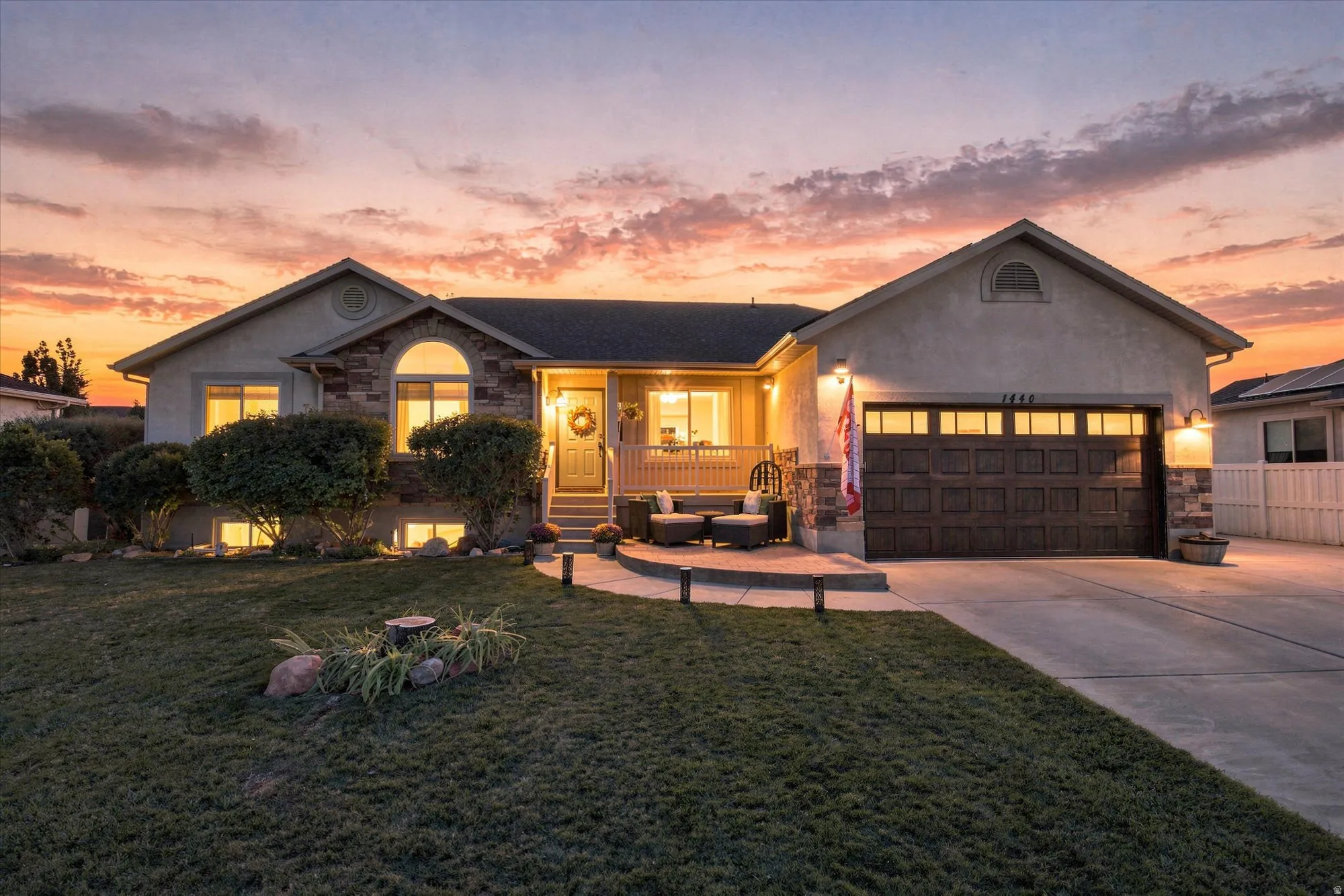 Stucco exterior with stone accents, covered front porch, arched window, attached garage with panel door, and concrete driveway