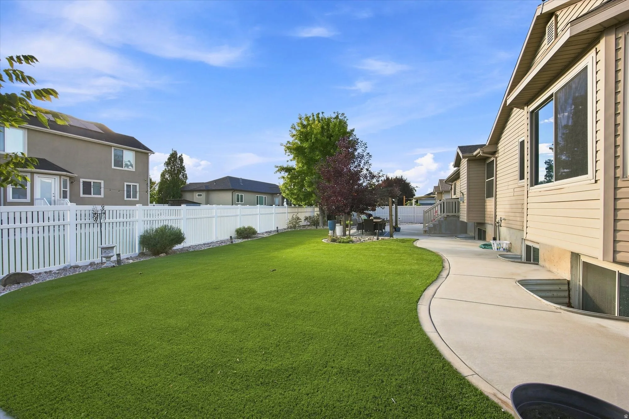 Expansive lawn area, concrete pathway, white picket fencing, established trees, and exterior siding