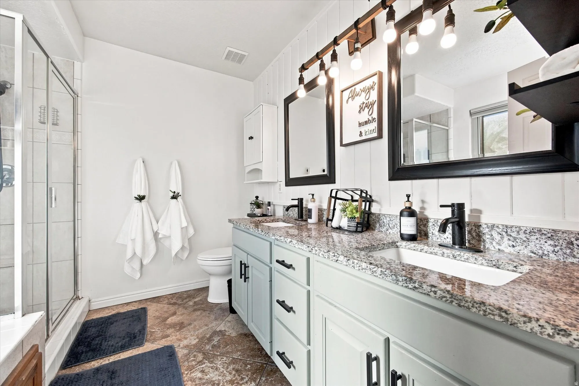 Dual vanity with granite countertops, light-toned cabinetry, and matte black fixtures