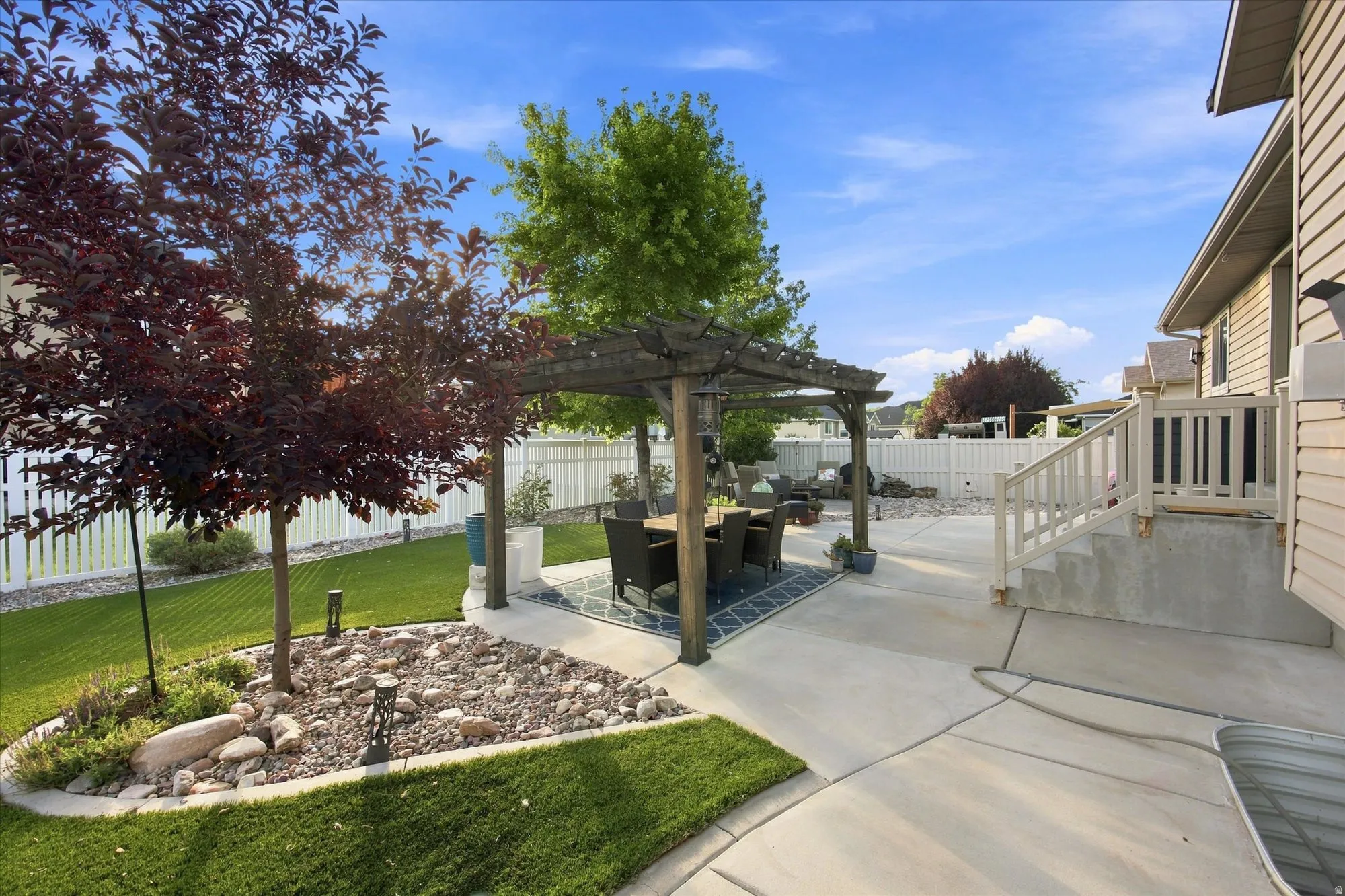 Expansive concrete patio featuring a pergola, manicured lawn, and mature trees