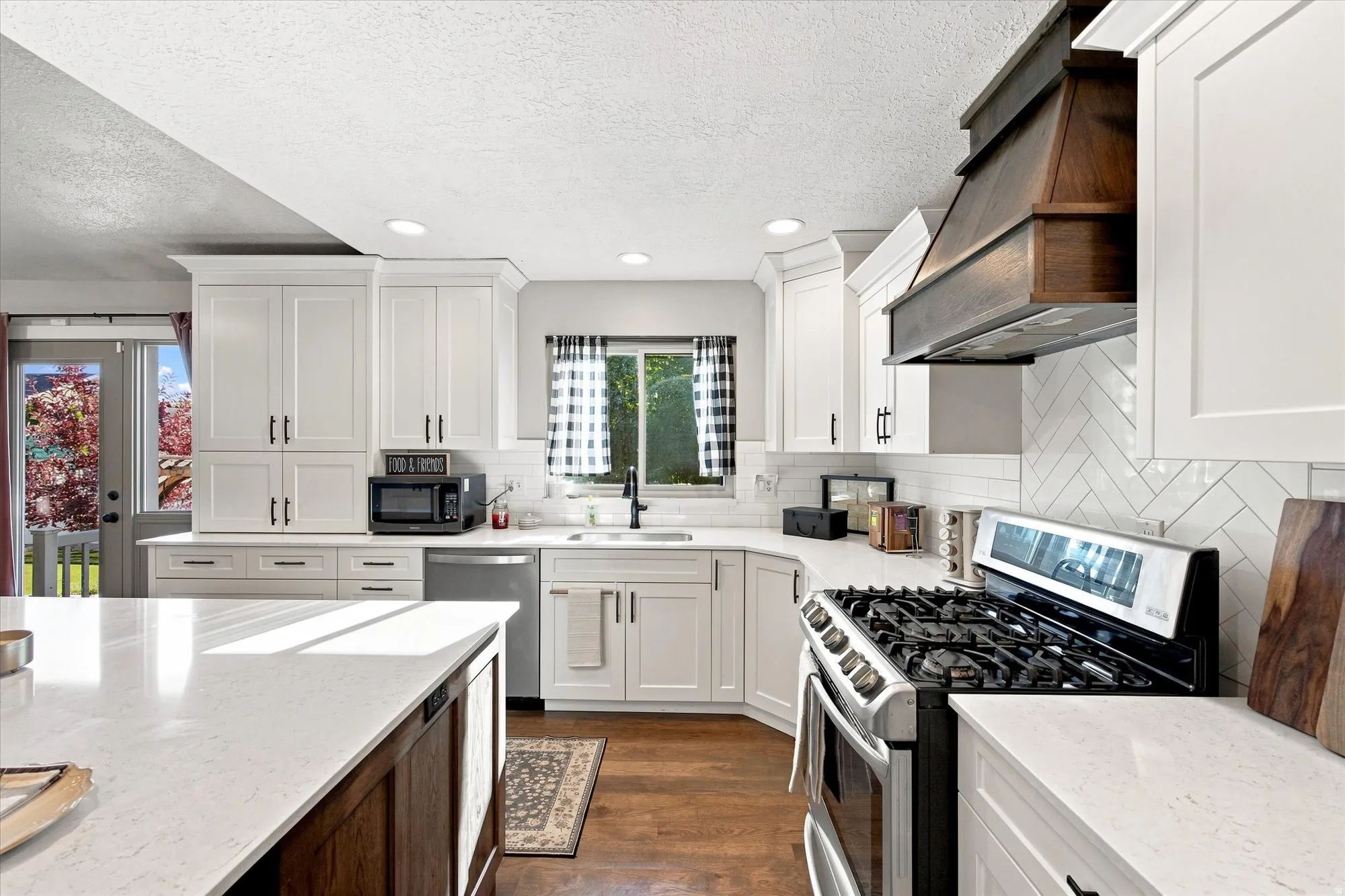 White shaker cabinetry, light-toned countertops, wood-finish flooring, a stainless steel range, and a wood range hood
