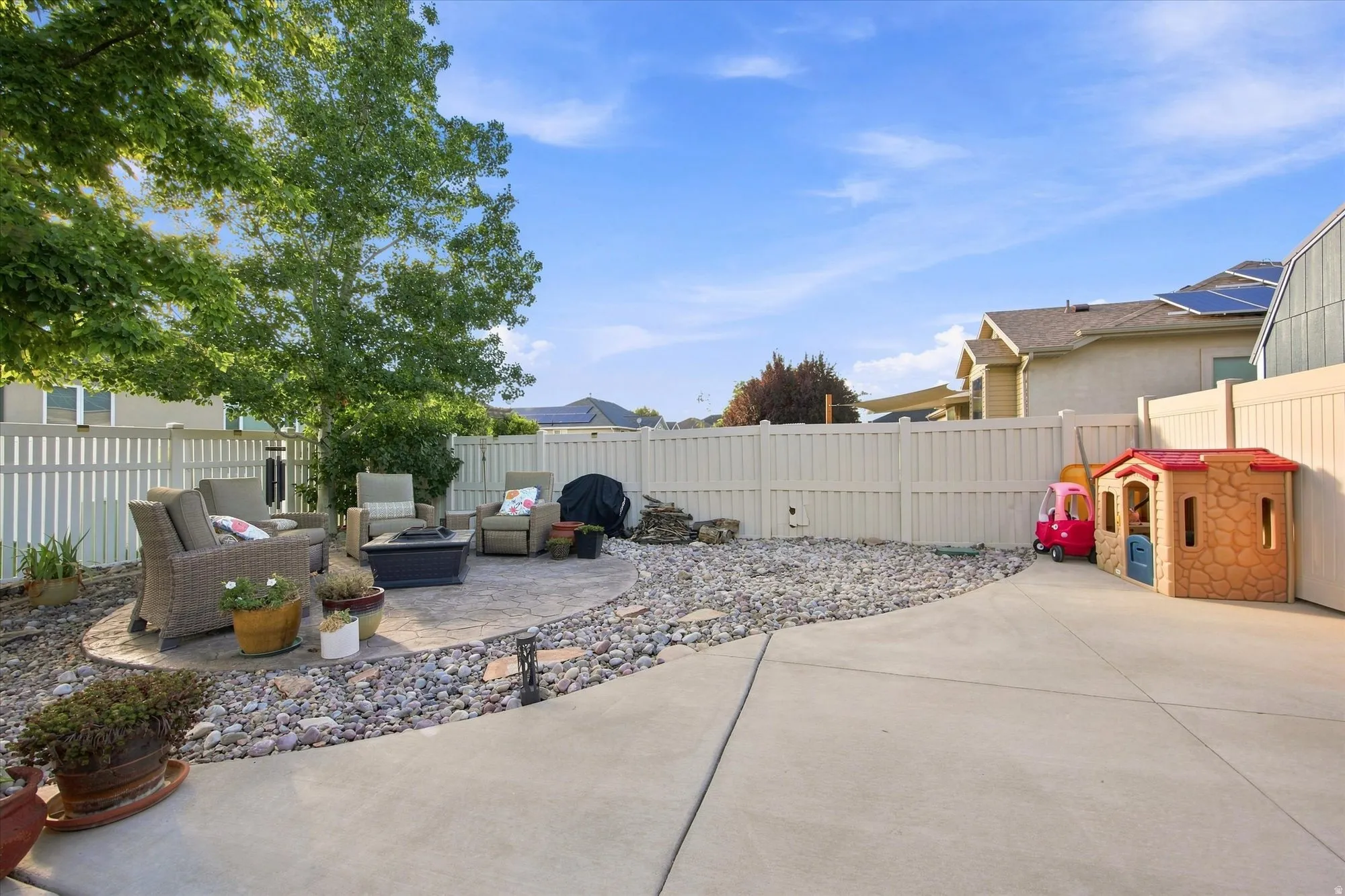 Expansive concrete patio with a circular paver seating area, surrounded by decorative rock landscaping
