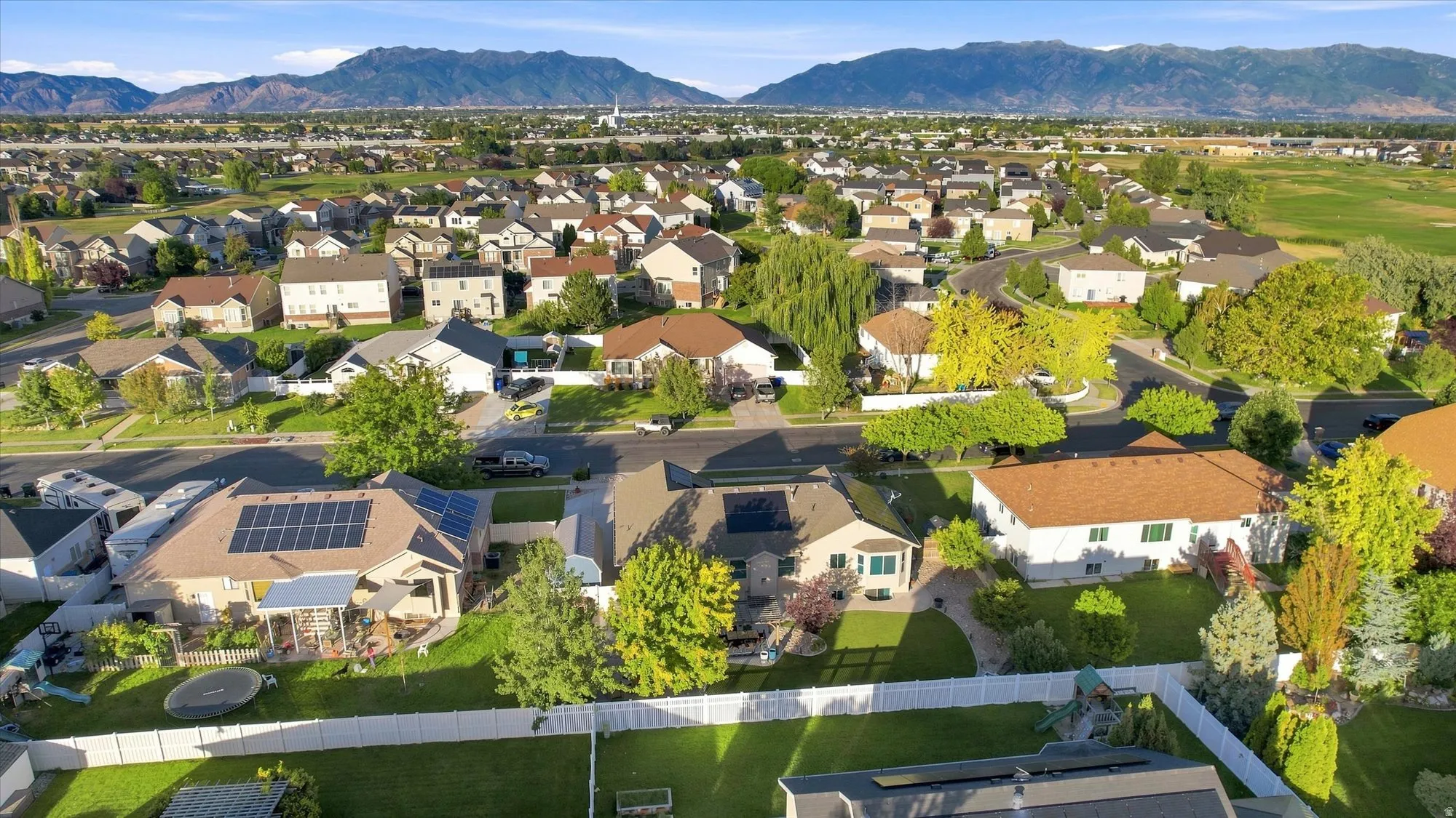 Expansive neighborhood setting with established homes, mature trees, mountain backdrop, and clear sky