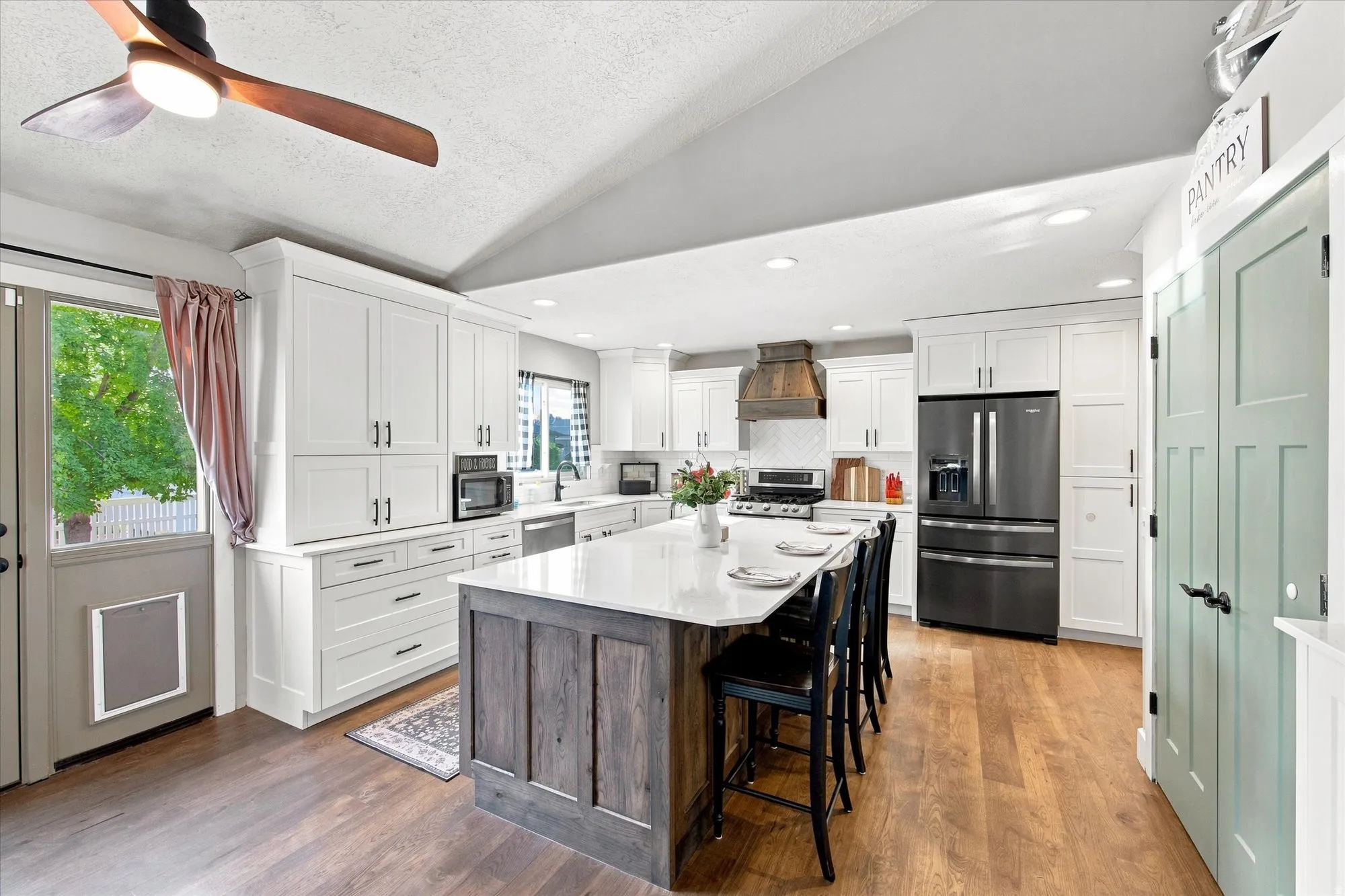 Kitchen featuring white shaker cabinetry, stainless steel appliances, a center island with countertop seating, wood-finish flooring, and a unique wood-clad range hood