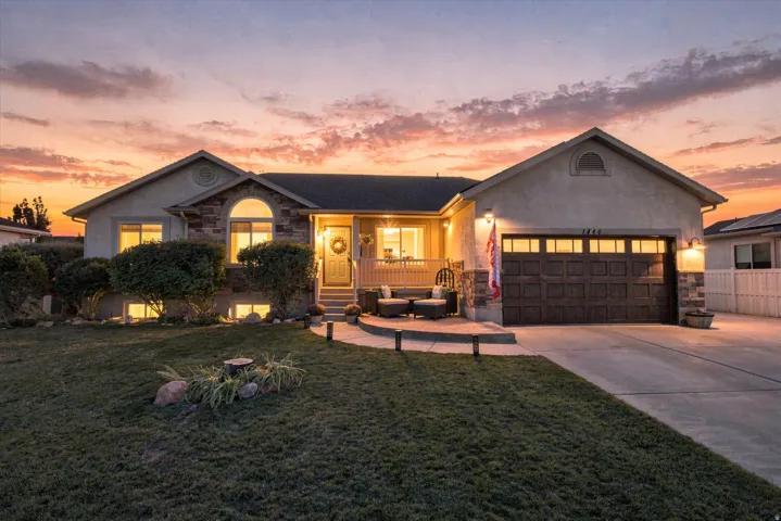 Stucco exterior with stone accents, covered front porch, arched window, attached garage with panel door, and concrete driveway