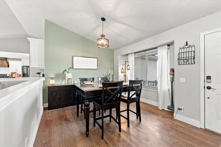 Wood-finish flooring throughout, a vaulted ceiling, and a large window with white curtains