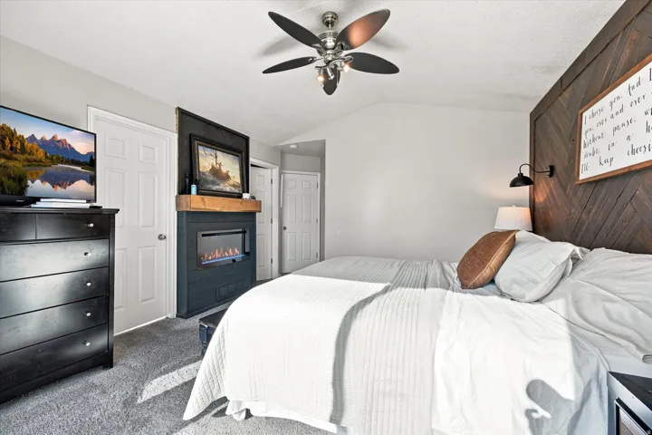 Built-in electric fireplace with wood mantel, ceiling fan with light fixture, and wood-paneled accent wall