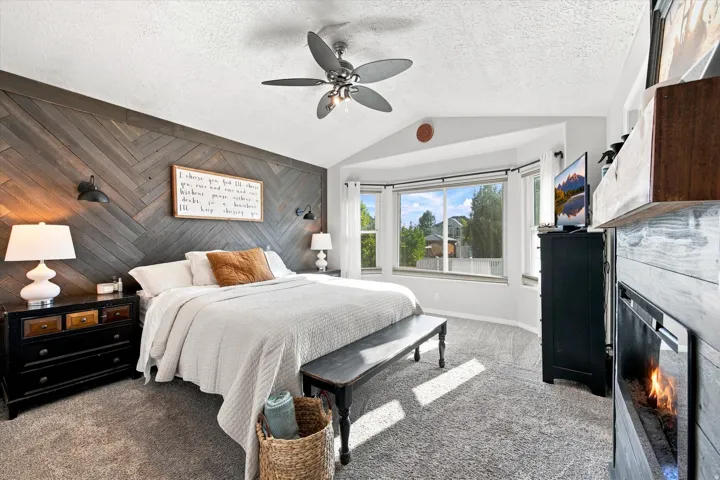 Vaulted ceiling with a ceiling fan, bay window, wood-finish accent wall, and a built-in fireplace