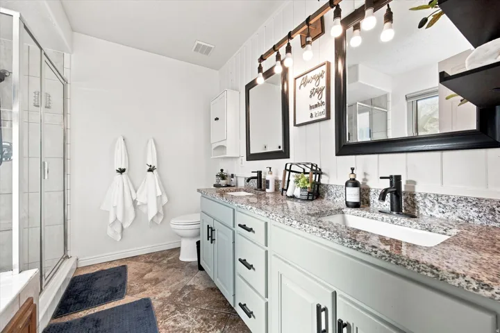 Dual vanity with granite countertops, light-toned cabinetry, and matte black fixtures