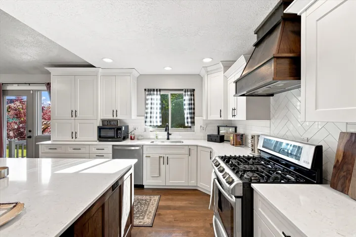 White shaker cabinetry, light-toned countertops, wood-finish flooring, a stainless steel range, and a wood range hood