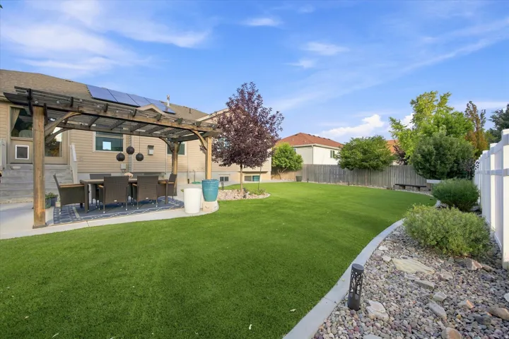 Expansive backyard featuring a manicured lawn, a wood pergola over a concrete patio, and mature landscaping with a decorative rock bed