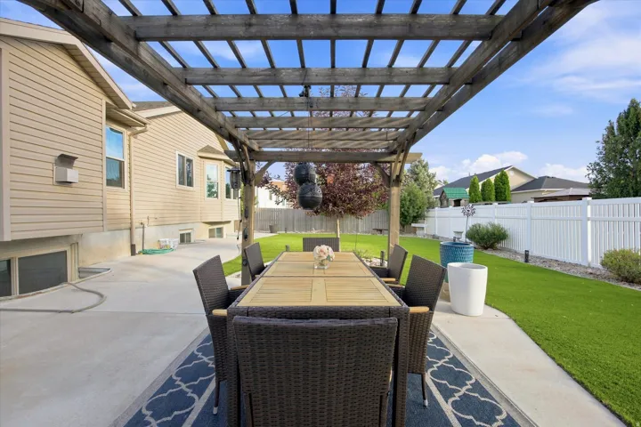 Spacious patio with a wooden pergola, concrete surfacing, and artificial turf