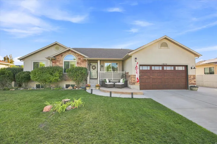 Stucco exterior with stone accents, covered front porch, arched window, attached two-car garage with wood-finish door, and concrete driveway