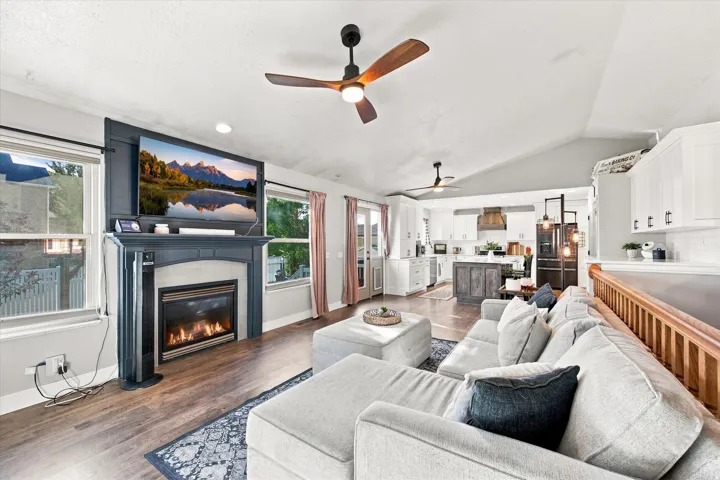 Vaulted ceiling, wood-finish flooring, built-in fireplace, ceiling fans, and a kitchen with white cabinetry