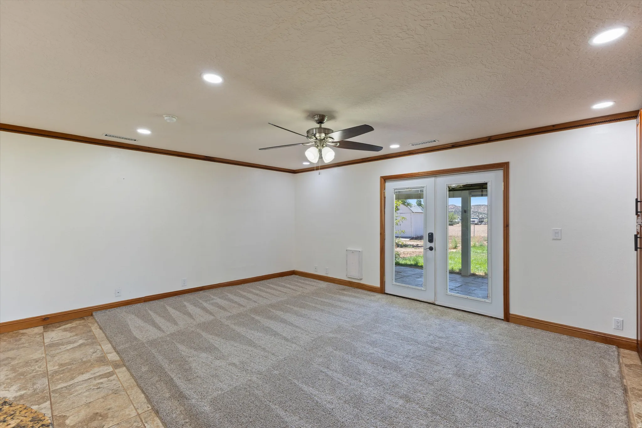 Recessed lighting, ceiling fan, carpet flooring, wood trim, and French doors leading to exterior stone patio