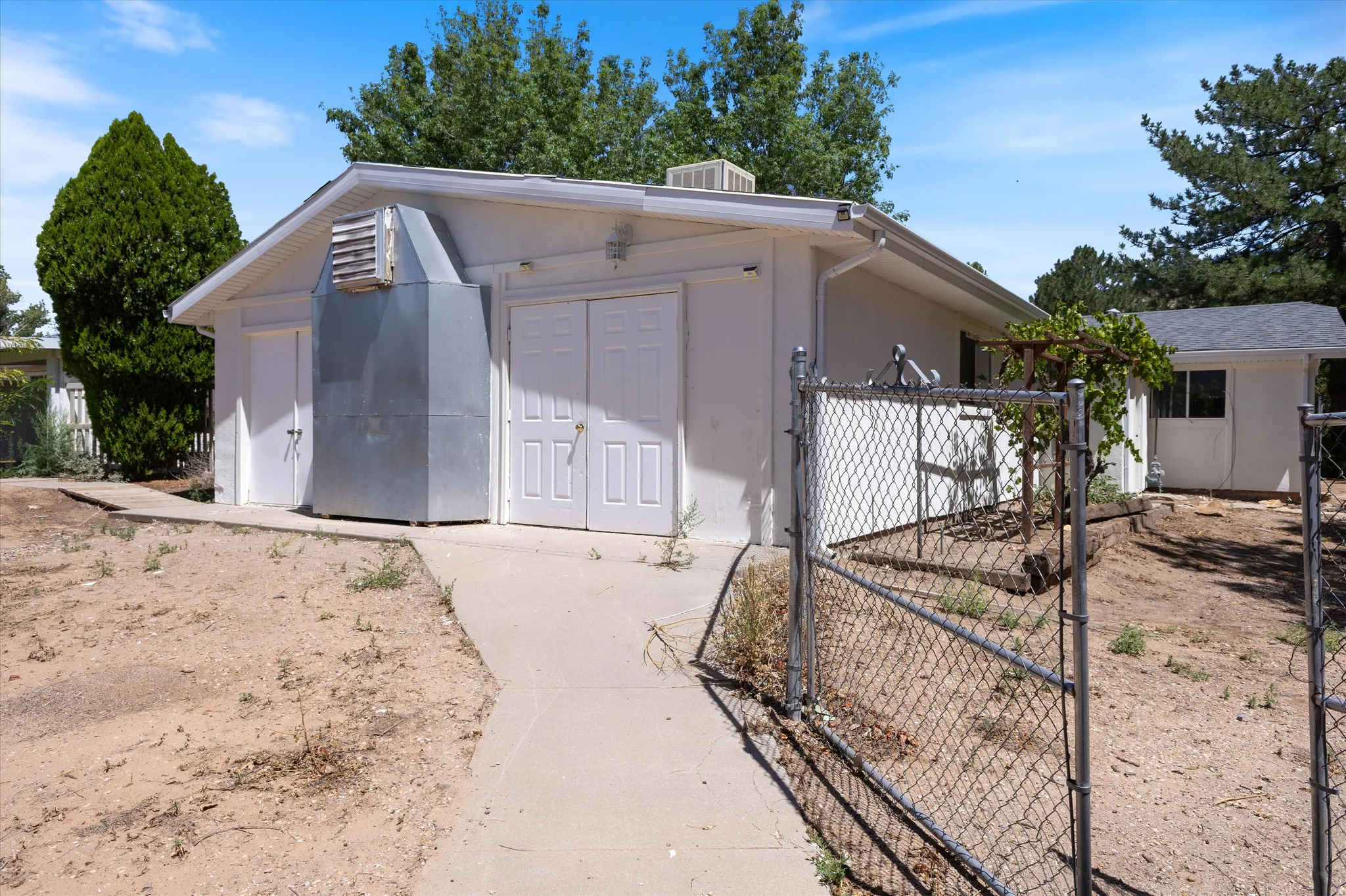 Detached structure featuring multiple access doors, a concrete pathway, and a chain-link fence