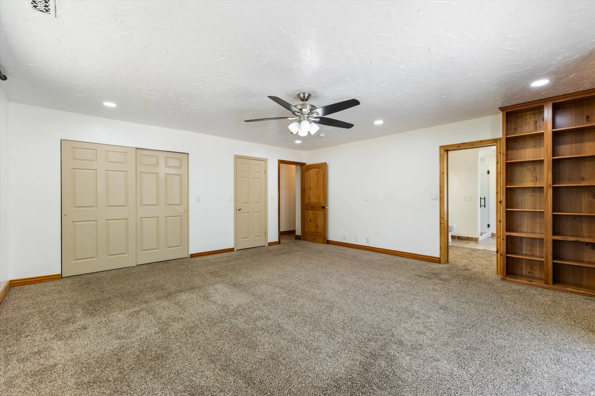 Spacious room featuring carpeting, a ceiling fan with light, recessed lighting, and built-in wood shelving