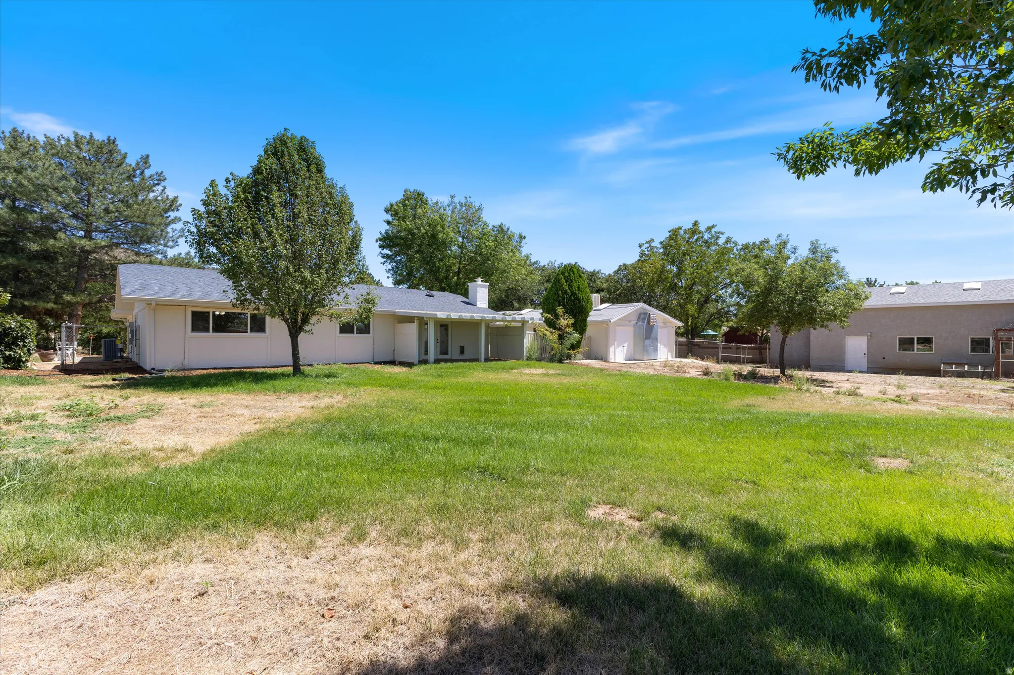 Expansive backyard featuring a manicured lawn, established trees, covered patio, and a separate storage shed