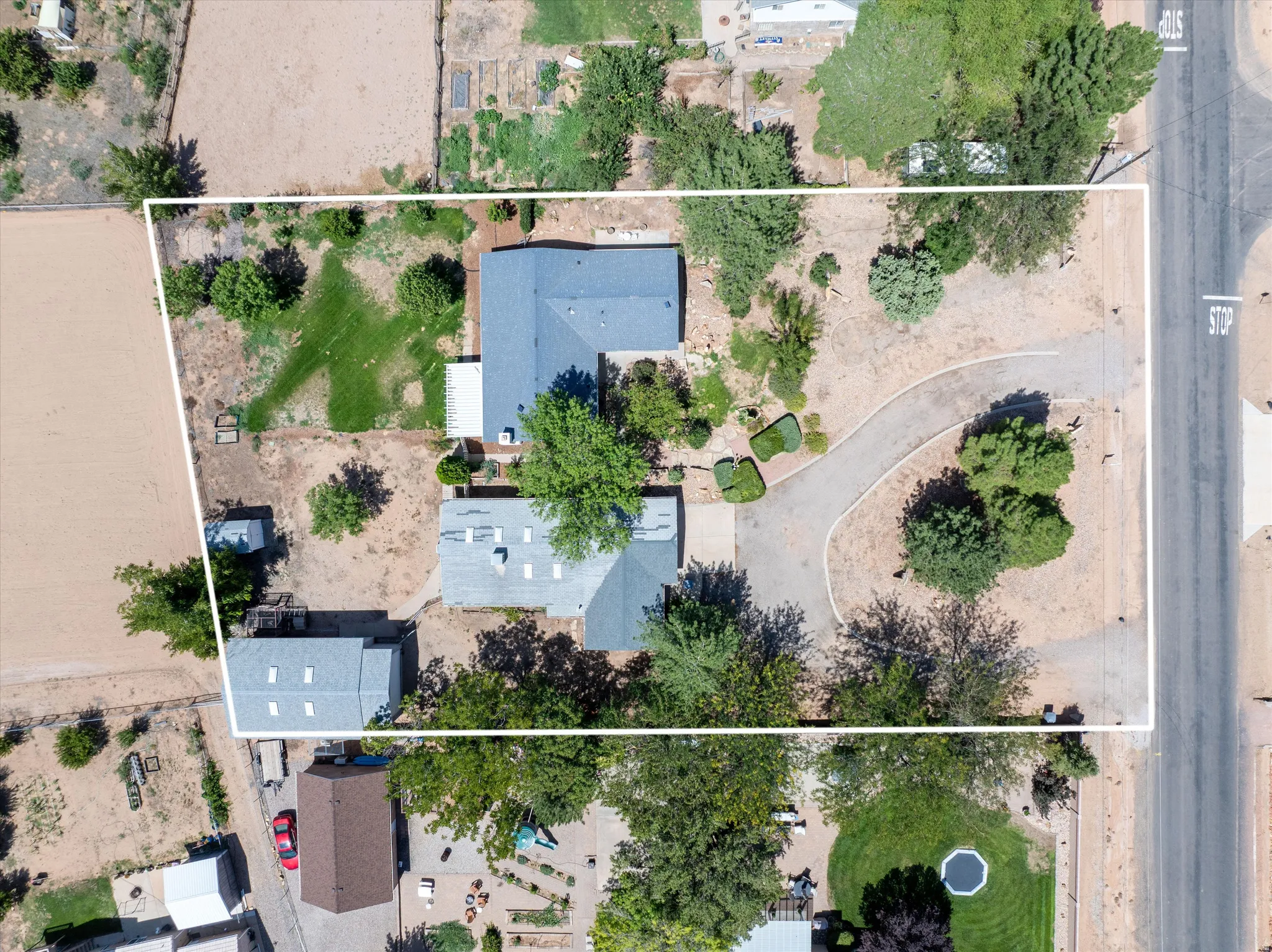 Expansive property featuring two structures, mature trees, a curved driveway, and a partially grassed area