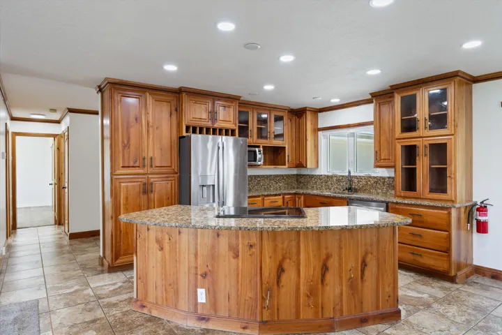 Kitchen with wood cabinetry, a center island with a cooktop, granite countertops, tile flooring, and recessed lighting