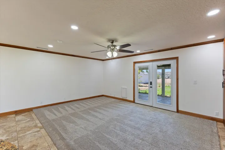 Recessed lighting, ceiling fan, carpet flooring, wood trim, and French doors leading to exterior stone patio