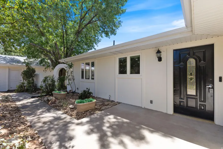 White stucco exterior with a black paneled entry door, decorative glass insert, and an exterior wall lantern