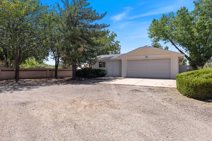 Single-story residence featuring a two-car garage, gravel driveway, mature trees, and a brick privacy wall